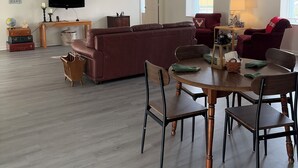 Un salón espacioso con un sofá grande, una mesa de comedor con sillas, un televisor montado en la pared y un candelabro en el techo.