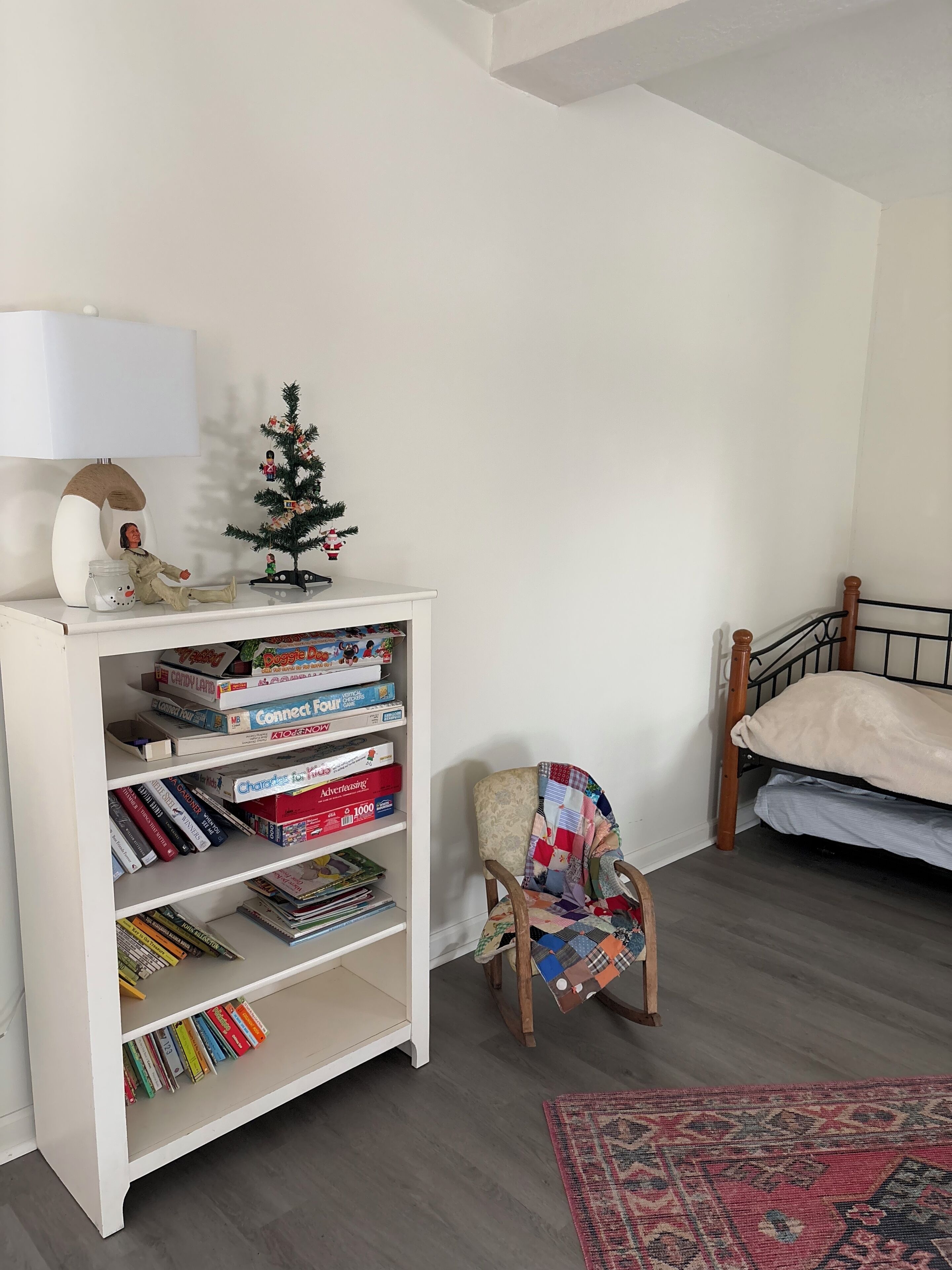 A room with a white bookshelf, a small Christmas tree, a chair, and a bed.