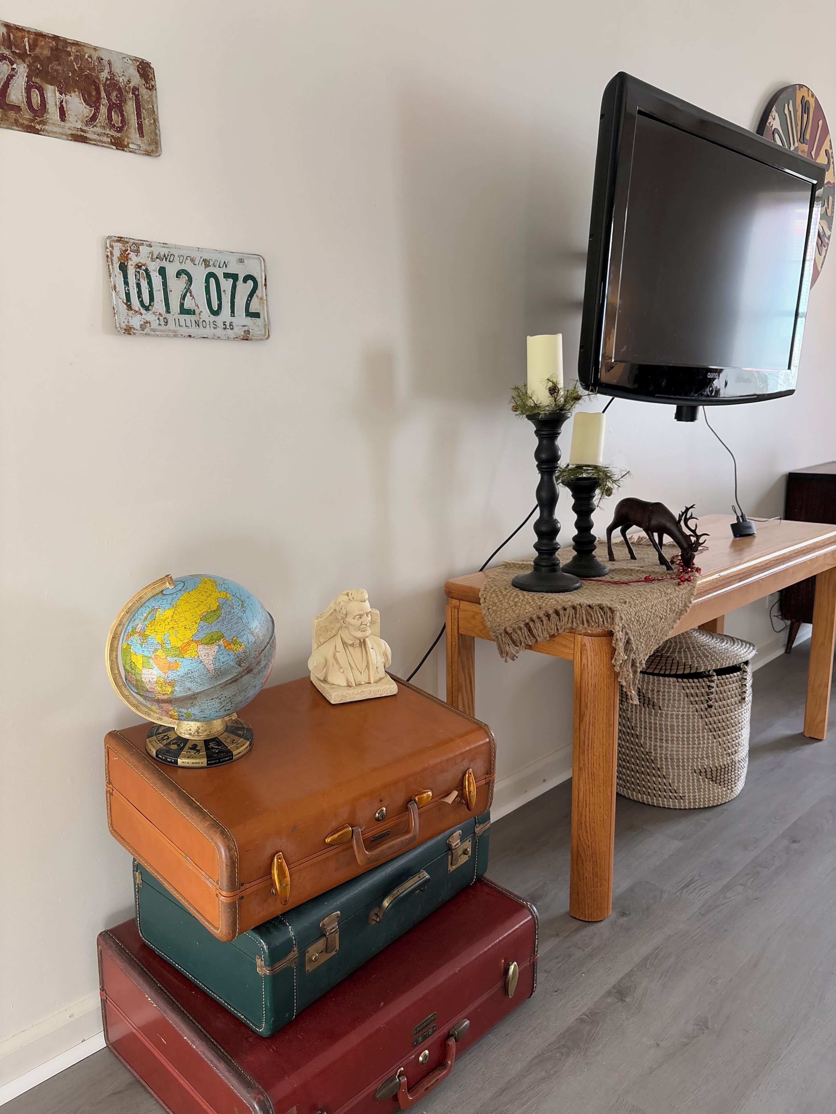 A room with a wooden table, a globe, vintage suitcases, a television, and decorative items.