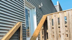 Una terraza de madera con una escalera que lleva a una casa con una puerta blanca y una ventana.