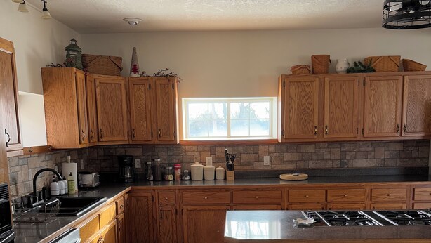 Cocina moderna con armarios de madera, una isla central con taburetes, una estufa integrada y un ventanal que proporciona luz natural.