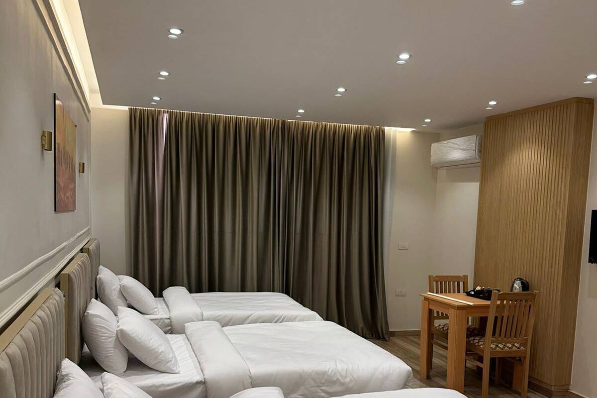 A hotel room with two beds, a wooden chair, a table, and a wall-mounted air conditioner.