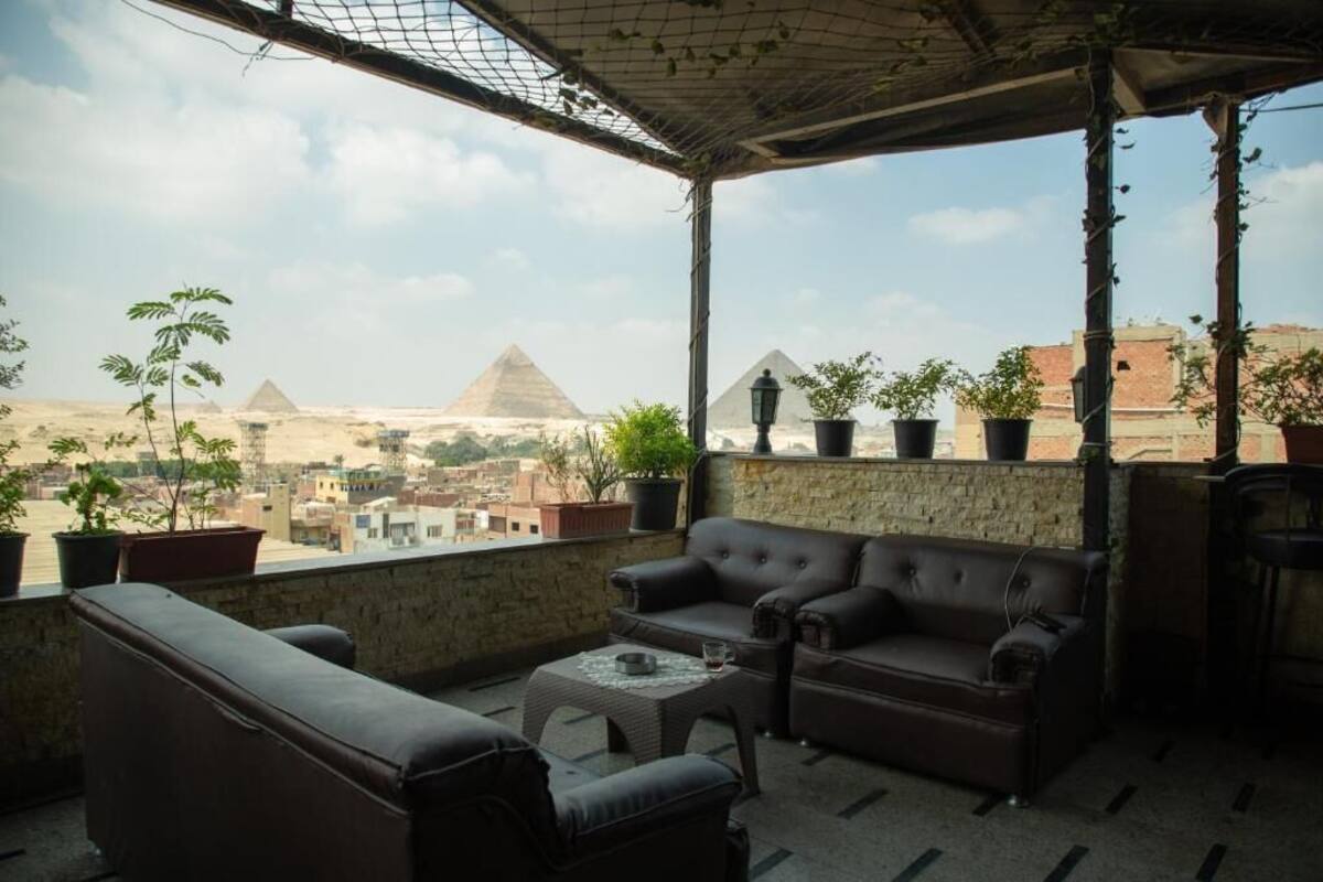 A balcony with a view of the pyramids, furnished with leather sofas and potted plants.