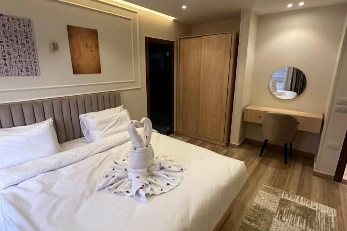 A hotel room with a large bed, a desk, a chair, a mirror, and a wardrobe.