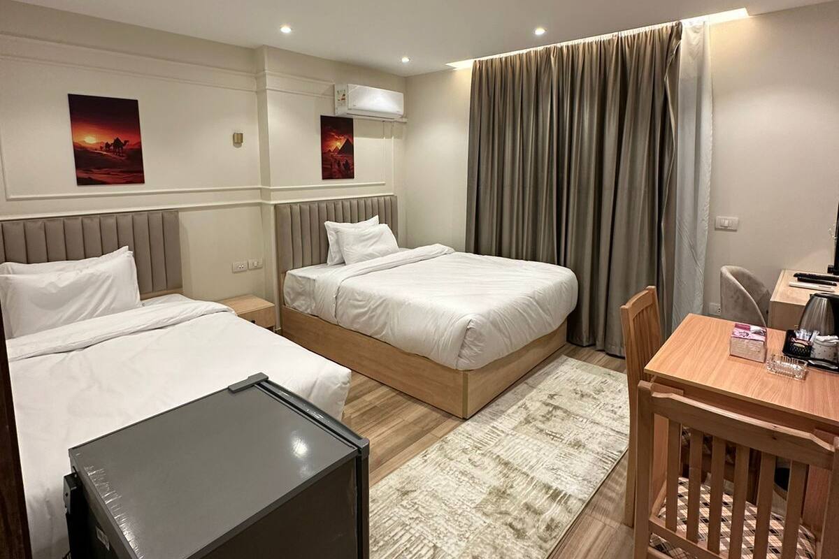 A hotel room with two beds, a desk, a chair, a small table, and a refrigerator.