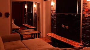 A modern hotel room with a large bed, a seating area with a table, and a TV mounted on a stone wall. - Cosy apartment with views over Paris (Le Kremlin-Bicêtre)
