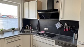 A modern kitchen with white cabinets, a black stove, and a window providing natural light. - Ferienwohnung am Weiher – Ihr perfektes Urlaubsdomizil für die ganze Familie! (Denklingen)