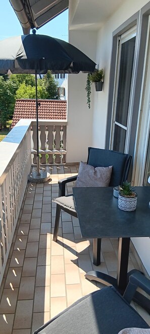 Un balcon avec une table et des chaises, une plante en pot et une plante suspendue.