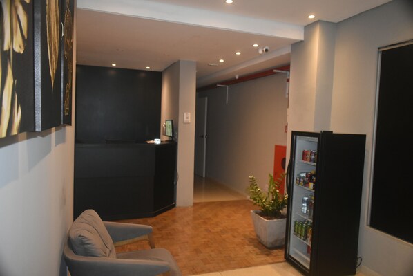 A hotel lobby with a reception desk, a seating area, a refrigerator stocked with beverages, and a potted plant. - Unity Hotel Paulista (São Paulo)