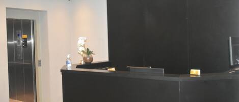 A reception area with a black reception desk, a potted plant, and an elevator in the background.