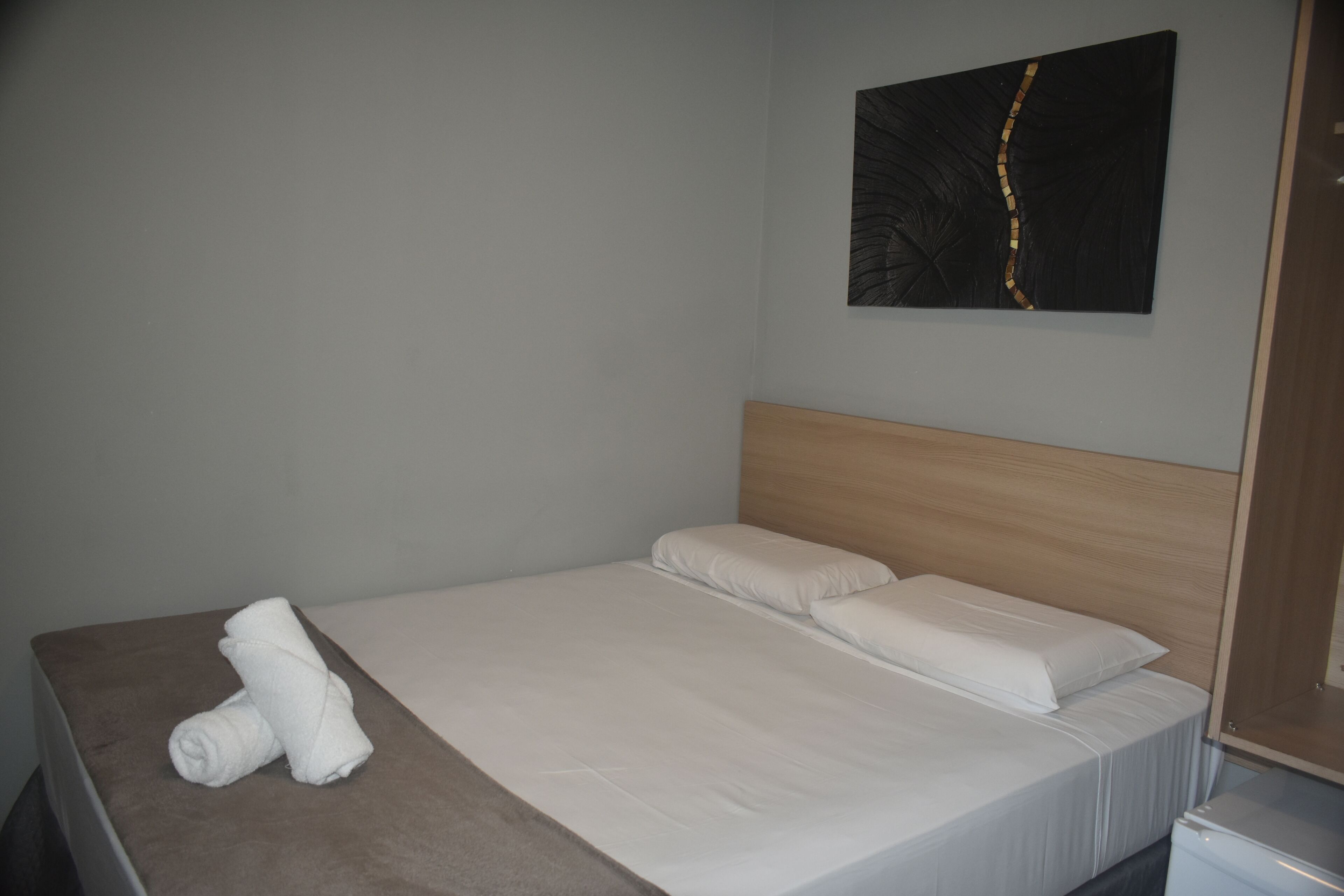 A neatly made bed with white linens and a rolled towel on the side.