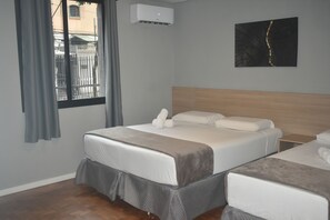 A hotel room with two beds, a wooden headboard, a gray wall, an air conditioning unit, and a window with curtains. - Unity Hotel Paulista (São Paulo)