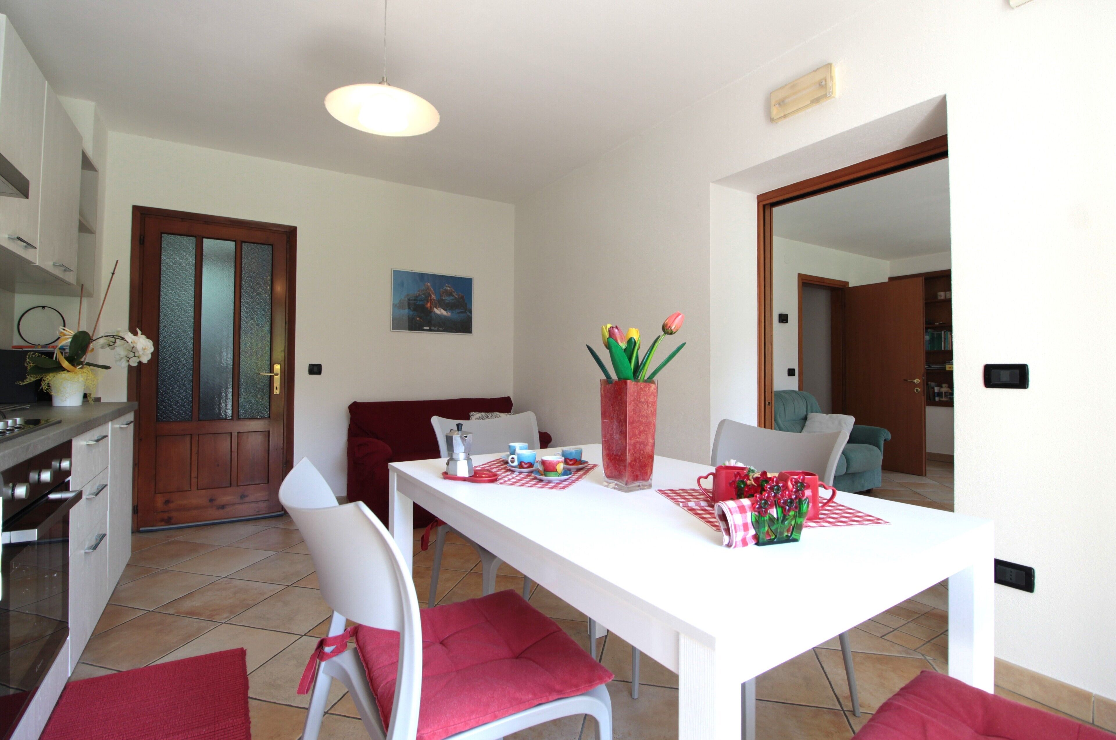 Un comedor con una mesa blanca, cojines rojos y un florero con flores.