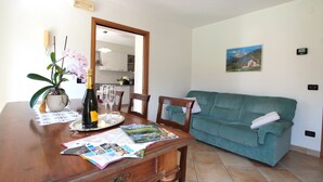 Een eetgedeelte met een houten tafel, stoelen, een groene bank, een potorkidee en een fles champagne.