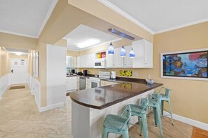 Una cocina con armarios blancos, encimera de granito e iluminación colgante azul.