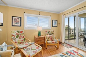 A room with two chairs, a small table, and a lamp. There is a window with blinds and a view of the outside. - 3 Bedroom Beachfront Condo with Pool and Hot Tub (Panama City Beach)