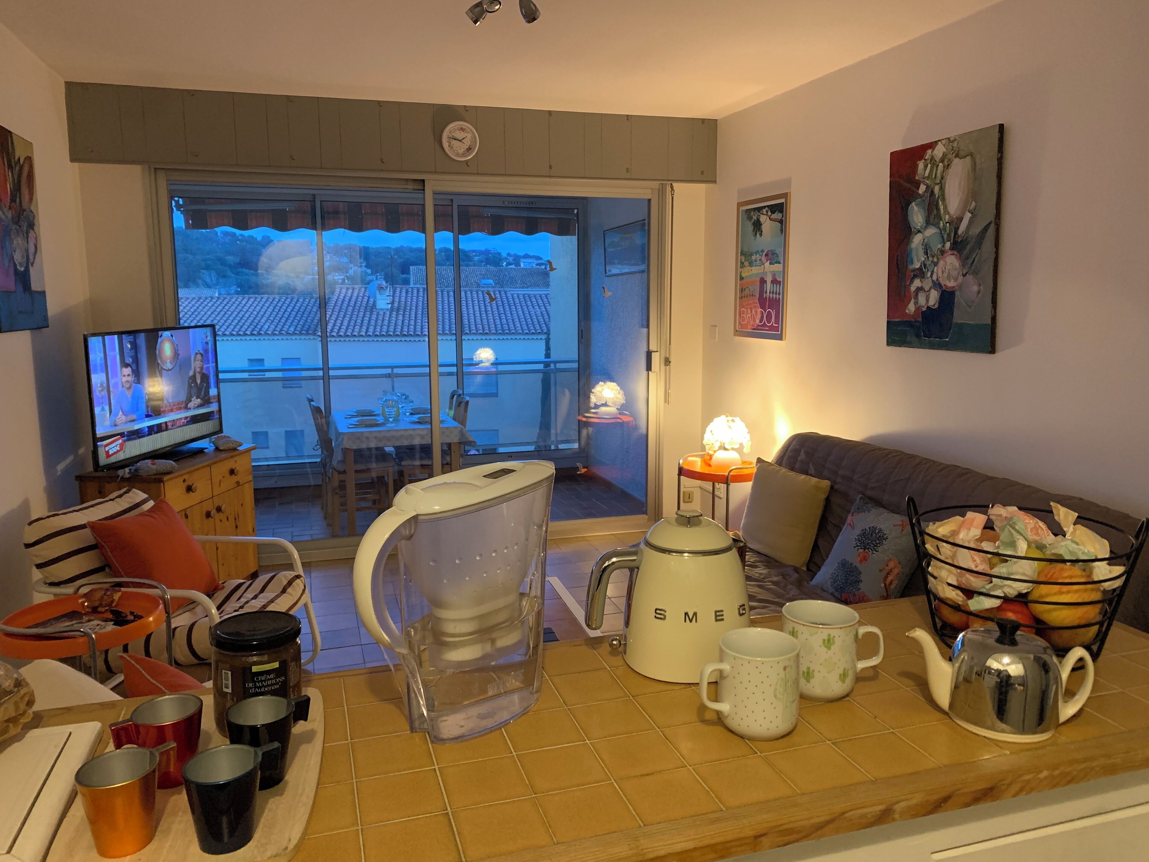 A cozy living room with a television, a coffee maker, and a dining area visible through the glass doors.