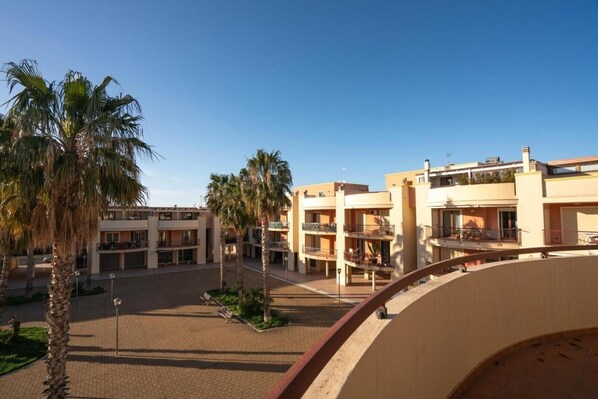 A courtyard with palm trees, a covered walkway, and multi-story buildings with balconies.