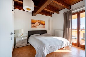 A bedroom with a bed, a nightstand, a lamp, a painting, a radiator, and a view through a glass door.