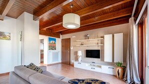 A living room with a sofa, TV, wooden ceiling, and a door leading to another room. - 'Attico da Mare 14' Apartment with Private Terrace, Wi-Fi and Air Conditioning (Polignano a Mare)