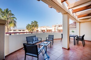 A terrace with outdoor seating, a table, and a view of buildings and palm trees.