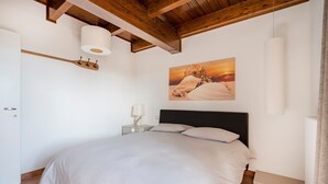 A bedroom with a large bed, wooden ceiling beams, a painting of a lion, and a bedside table with a lamp. - 'Attico da Mare 14' Apartment with Private Terrace, Wi-Fi and Air Conditioning (Polignano a Mare)