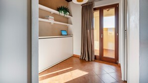 A room with a white desk, shelves with books and a plant, a laptop, a large window with curtains, and a wooden ceiling. - 'Attico da Mare 14' Apartment with Private Terrace, Wi-Fi and Air Conditioning (Polignano a Mare)