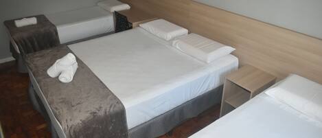 A hotel room with three single beds, each with a wooden headboard and a small bedside table.