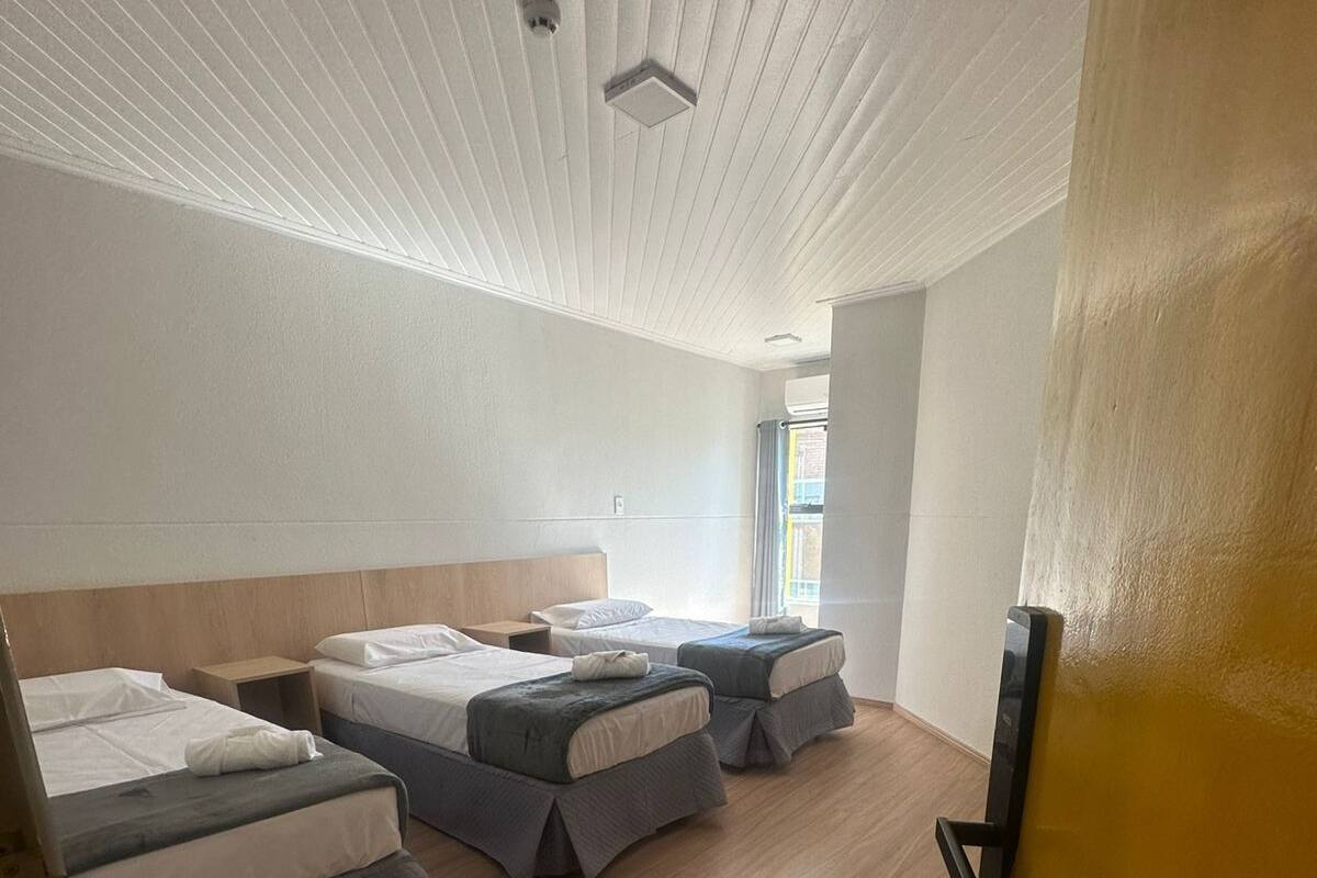 Ett hotellrum med tre sängar, trägolv och ett vitt tak med en ventilationsöppning.