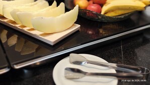 A kitchen counter with a cutting board holding sliced fruit, a bowl of mixed fruit, and a spoon. - Unity Hotel Votorantim (Votorantim)