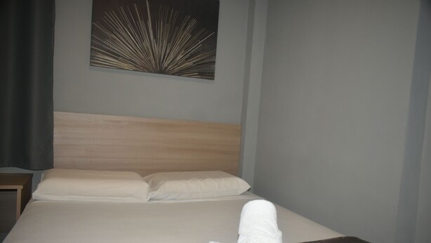 A neatly made bed with a wooden headboard, a single white pillow, and a brown throw blanket. - Unity Hotel Votorantim (Votorantim)