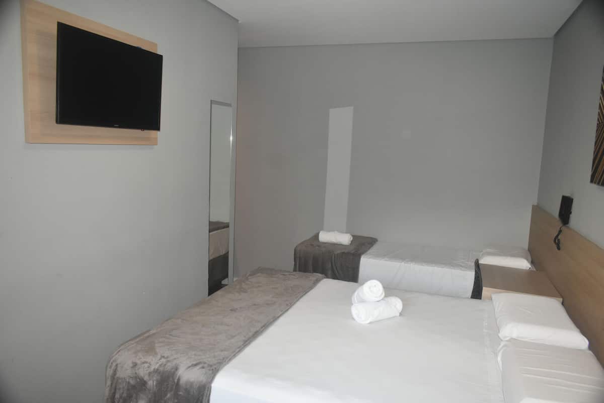 Ett hotellrum med två separata sängar, en platt-TV som är monterad på väggen och en sänggavel i trä.