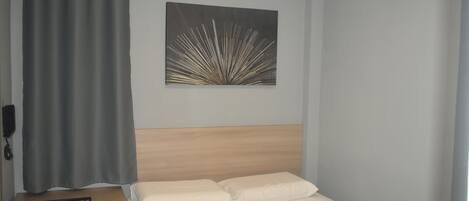 Un dormitorio con cama, cabecero, aire acondicionado instalado en la pared, cortina y un cuadro.