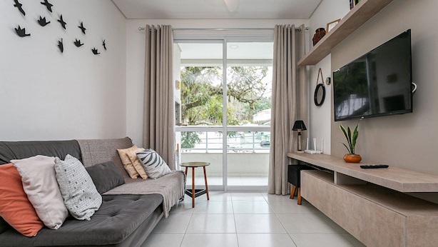 A modern living room with a grey sofa, a small round table, and a TV mounted on a wall.