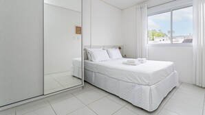 A modern bedroom with a large bed, a wardrobe, and a window with curtains.
