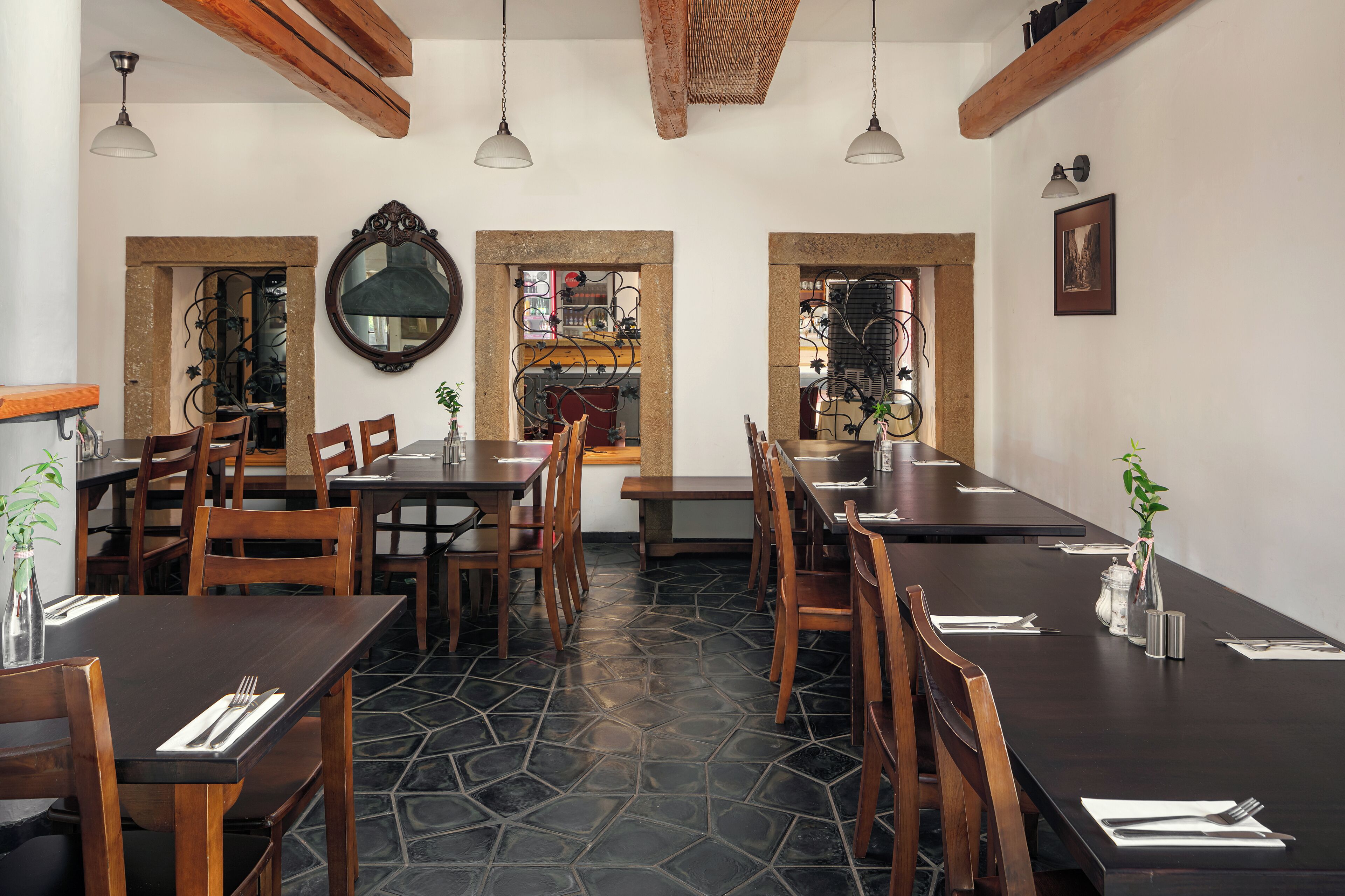 Un restaurant avec des tables et des chaises en bois, un sol en pierre et des luminaires suspendus.