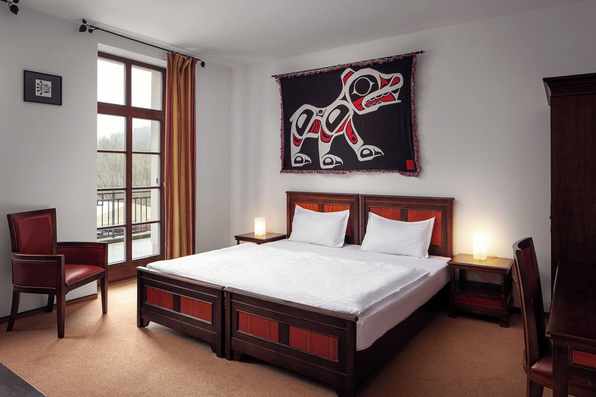 A hotel room with a large bed, two bedside tables, a chair, and a window with curtains.