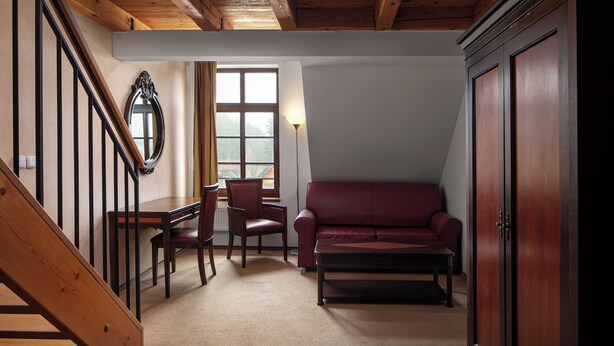Une pièce avec un escalier en bois, un canapé en cuir rouge, une table à manger avec des chaises et une grande armoire en bois.