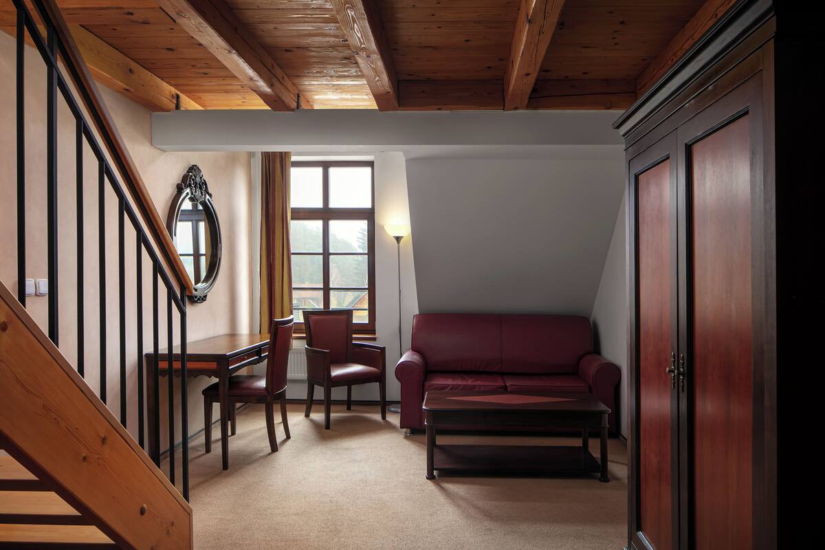 A room with a wooden staircase, a red leather sofa, a dining table with chairs, and a large wooden cabinet.