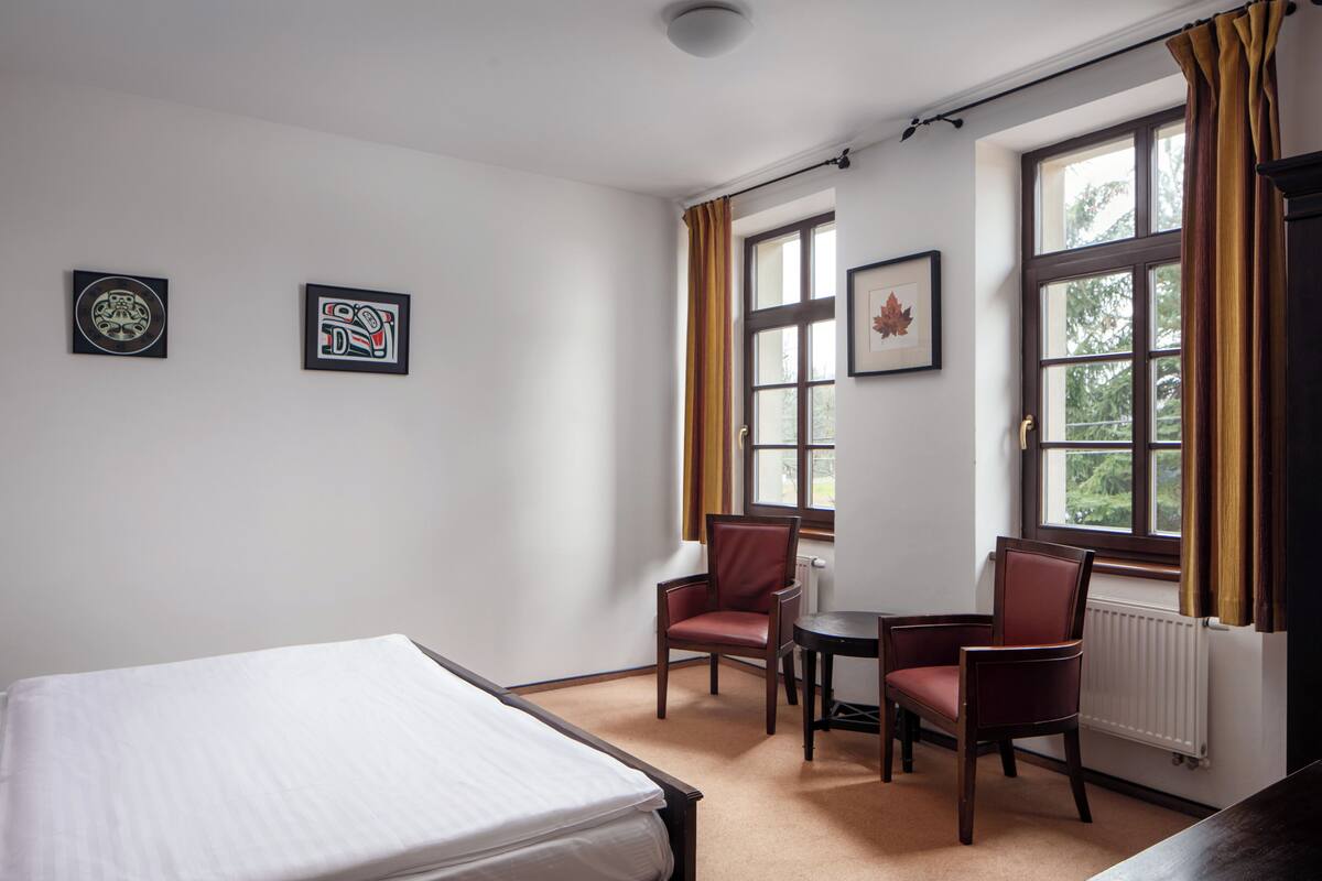 A hotel room with a bed, two chairs, a small table, and a window with curtains.