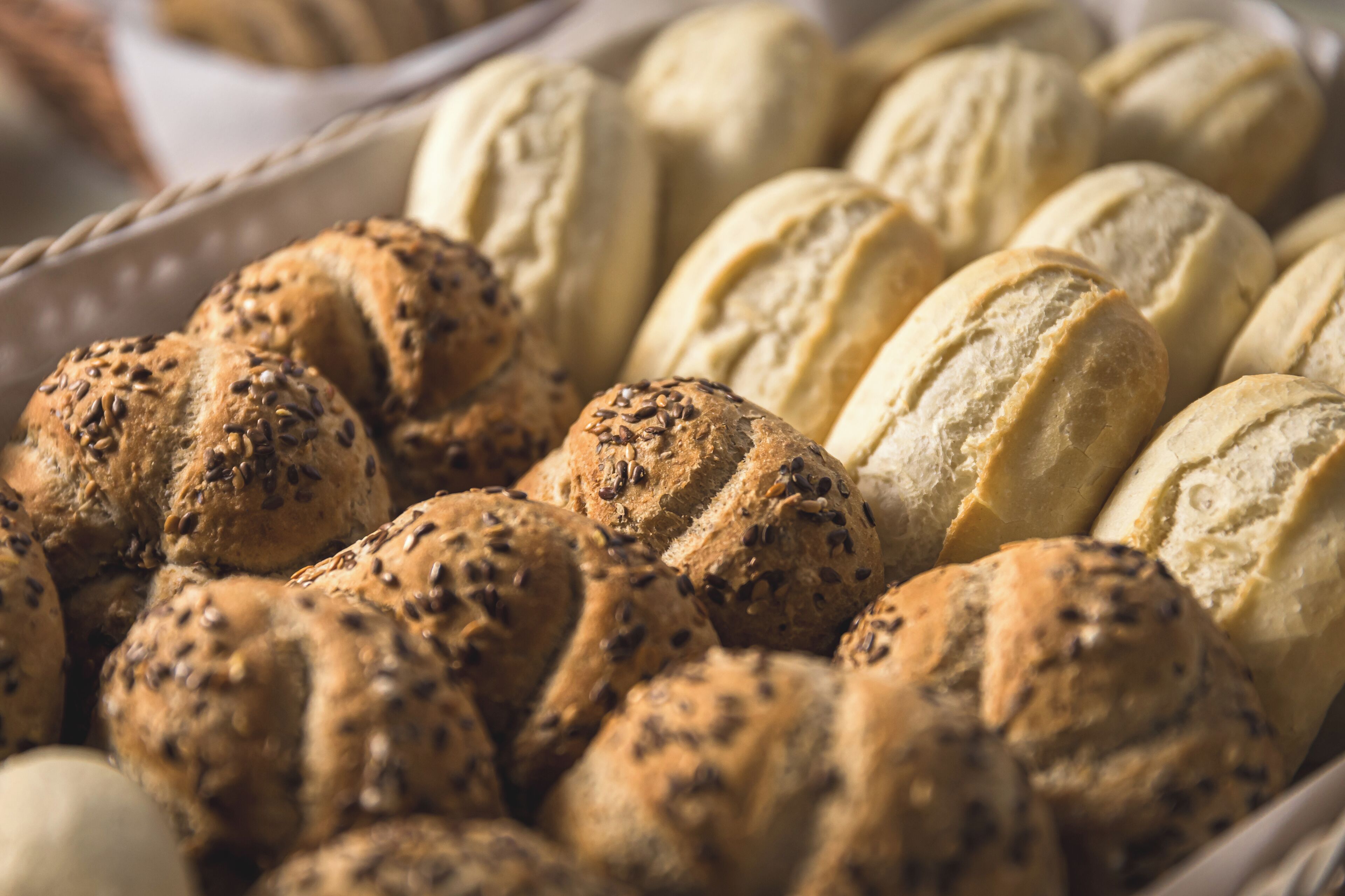 A basket filled with various types of bread, including seeded and plain varieties.