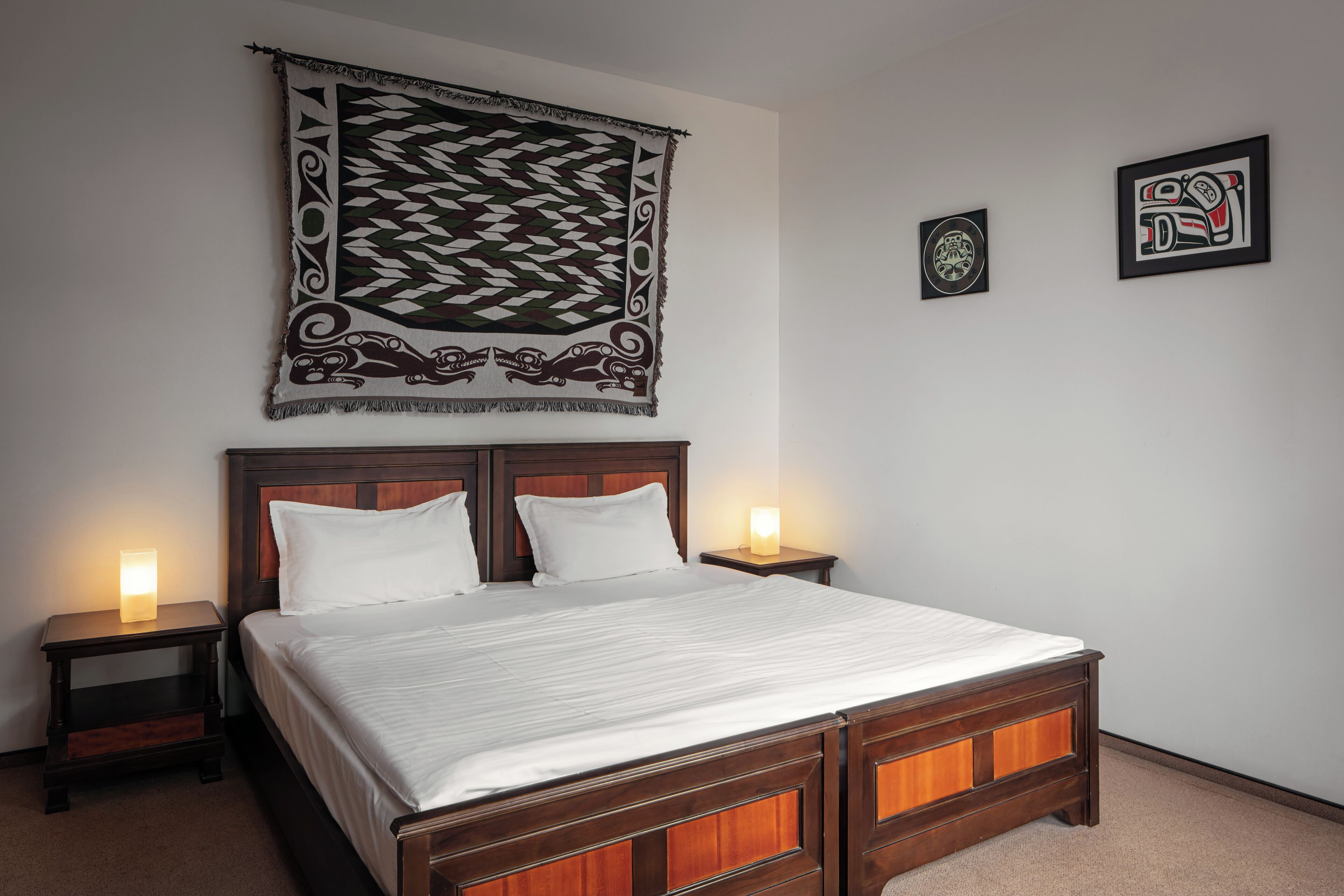 A neatly made bed with a wooden headboard, two bedside tables with lamps, and a tapestry hanging above.
