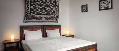 A neatly made bed with a wooden headboard, two bedside tables with lamps, and a tapestry hanging above.