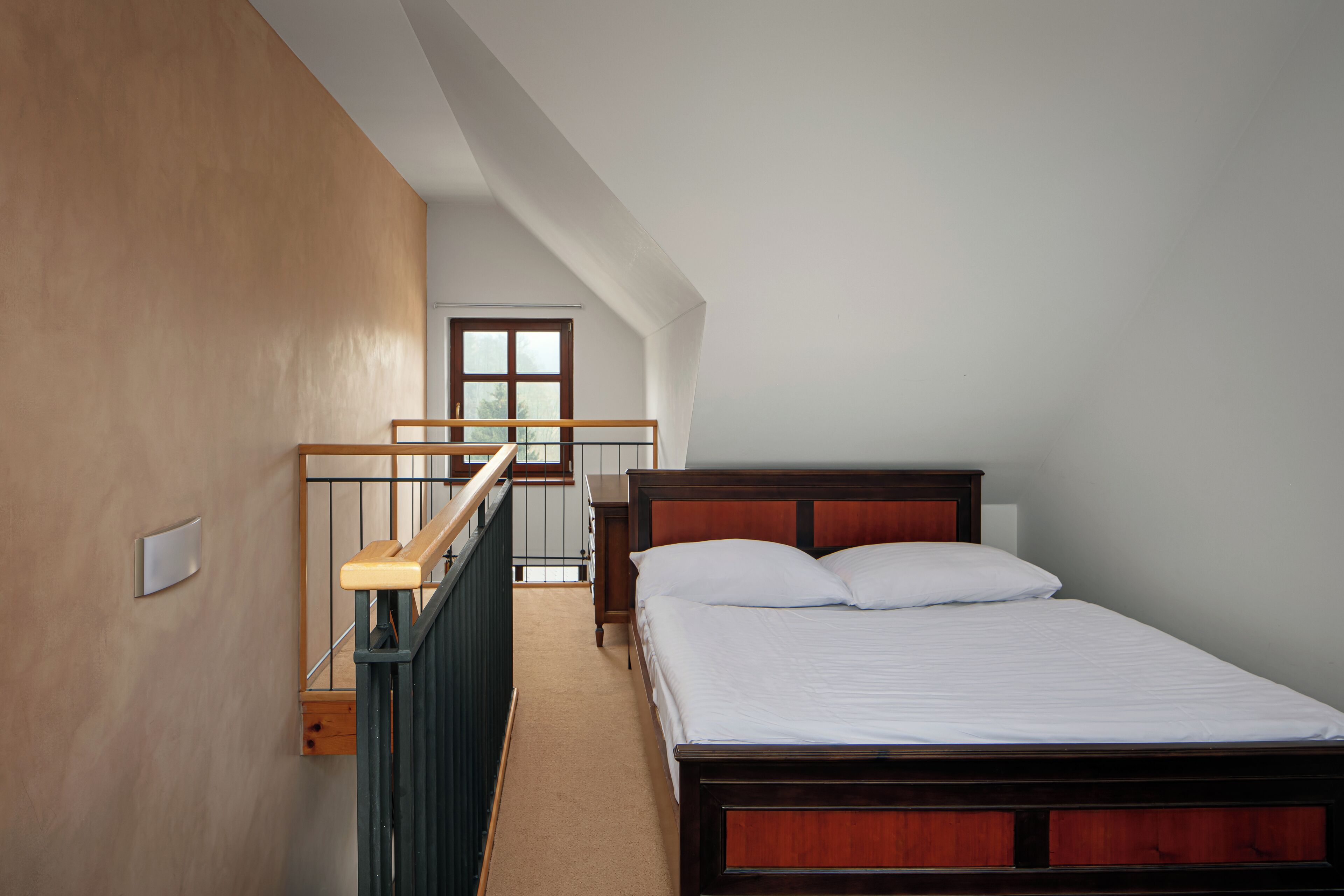 Quarto com cama de madeira, janela e escada que leva a um andar superior.
