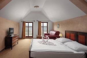 Una habitación de hotel con una cama bien hecha, un televisor en una cómoda, un sillón rojo y una ventana con cortinas.