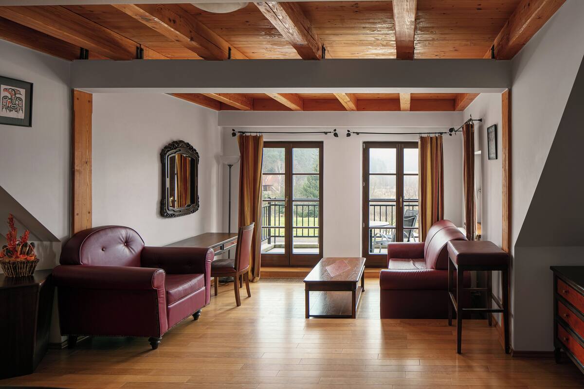 A spacious living room with wooden flooring, a fireplace, and large windows with curtains.
