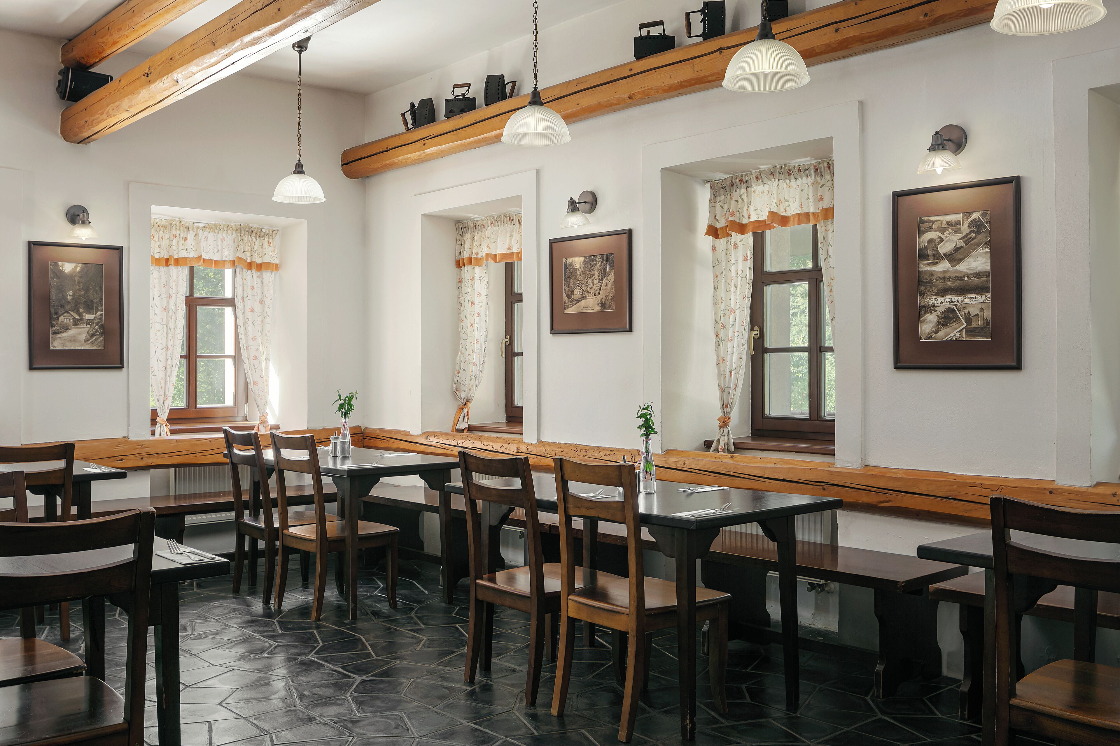 A restaurant with wooden tables and chairs, stone flooring, and framed pictures on the walls.