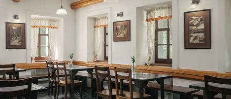 A restaurant with wooden tables and chairs, stone flooring, and framed pictures on the walls.