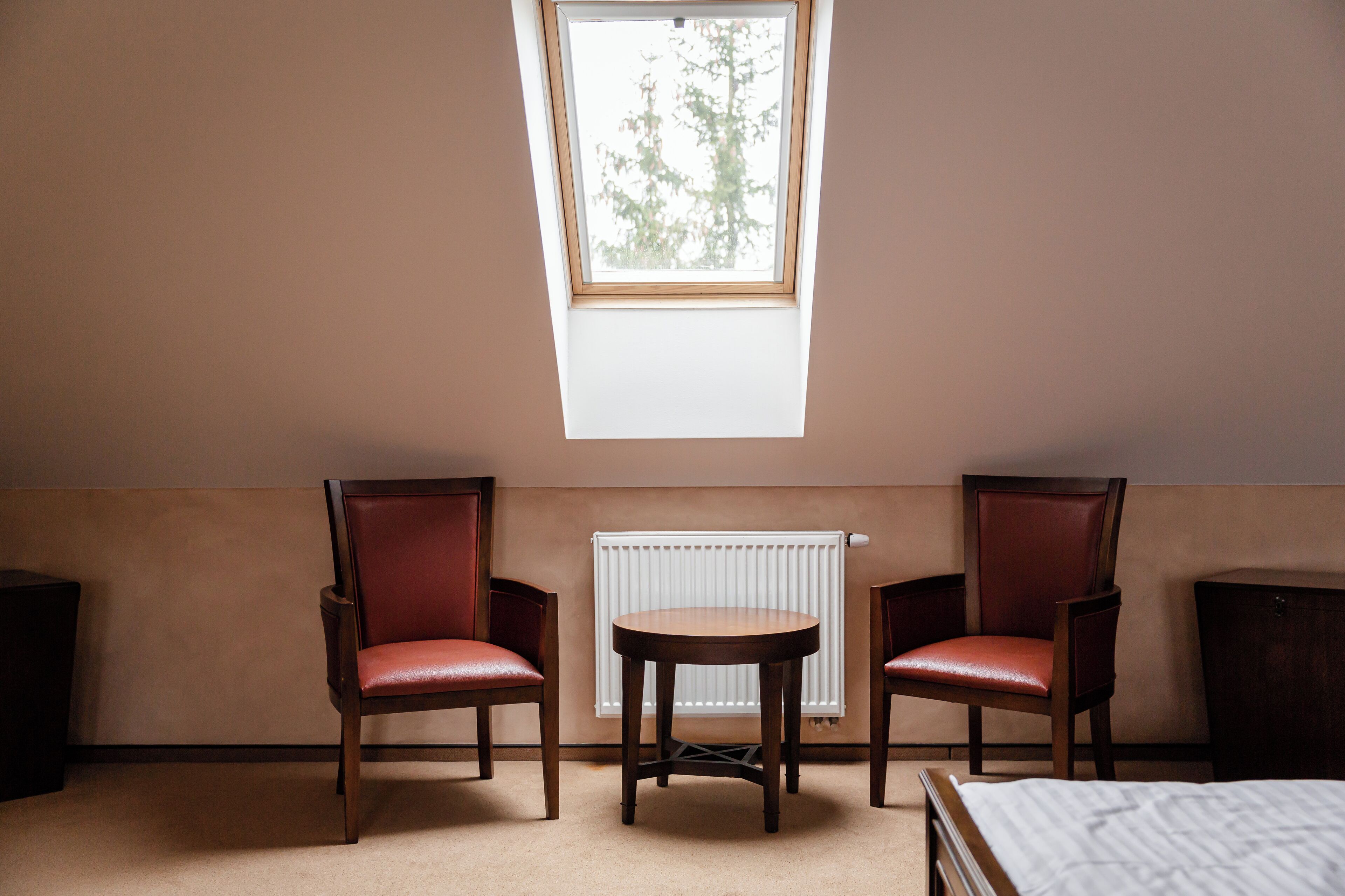 A room with two wooden chairs, a small round table, and a skylight above.