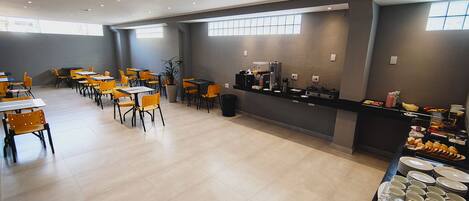 Un comedor amplio con varias mesas y sillas, una estación de café y un bufé con diversas opciones de comida.